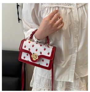 Close-up of strawberry print handbag with red woven handle and gold floral twist lock