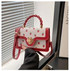Close-up of strawberry print handbag featuring gold floral clasp and red spiral handle