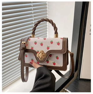 Detail of strawberry print bag with gold flower twist lock and woven brown handle