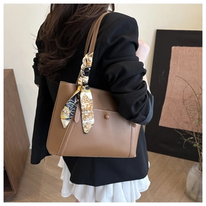 Close-up of brown leather tote bag with decorative silk scarf and stitched pocket detail