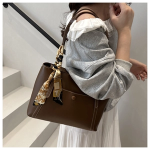 Detail of a brown leather tote bag with white contrast stitching and a silk scarf handle