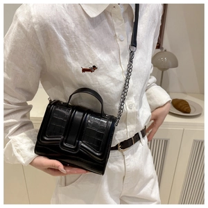 Detail of black crocodile texture bag with silver chain strap on a model indoors