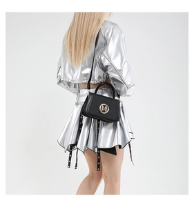 Detail of trendy black crossbody bag with gold M-letter logo worn by a fashion model