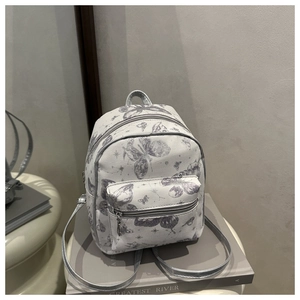 Detail of mini white backpack with grey butterfly print and silver straps on a book