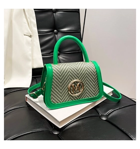 Dettaglio borsa a tracolla intrecciata verde con logo M dorato su elegante libro bianco