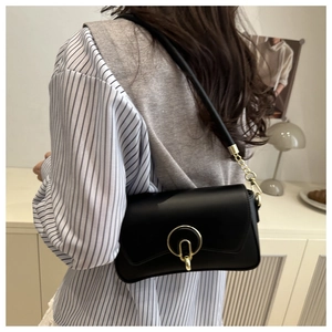 Detalle de bolso negro bajo el brazo con hebilla dorada y cadena llevado por una modelo