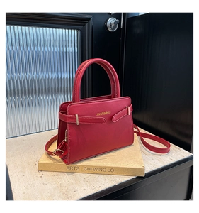 Detail van rode leren crossbodytas met gouden hardware en logo op vintage boeken