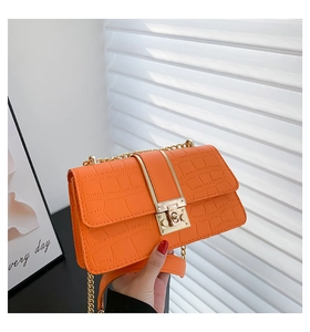 Detail van helder oranje handtas met krokodillenreliëf, gouden ketting en slot