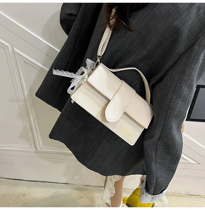 Close-up of cream crossbody bag with pearl lace charm on a stylish grey blazer