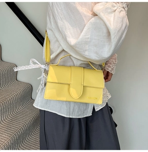 Detail of yellow crossbody bag featuring fashion embossing and lace bow with pearl charm