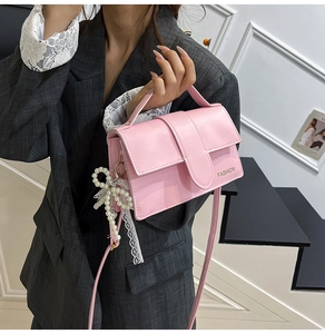 Pink leather handbag with golden Fashion text and pearl bow charm shown in hand