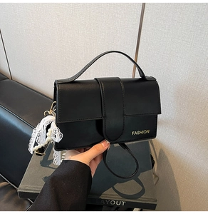 Detail of black PU leather crossbody bag featuring gold lettering and pearl lace bow charm