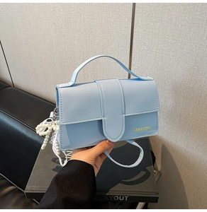 Close-up of a light blue rectangular PU leather bag with gold fashion text and pearl charm