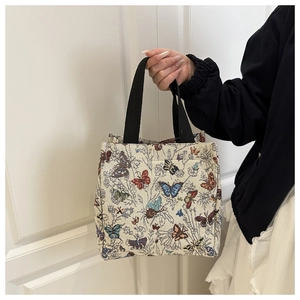 Close-up of a woven tote bag featuring colorful butterfly patterns and black handles