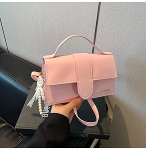 Pink faux leather handbag detail with gold 'FASHION' text and pearl bow charm