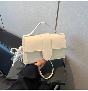 Close-up of cream crossbody bag with pearl charms and lace bow on a textured surface