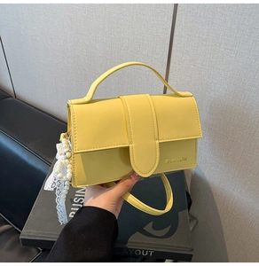 Detail view of bright yellow mini crossbody bag with pearl lace bow charm and fashion logo