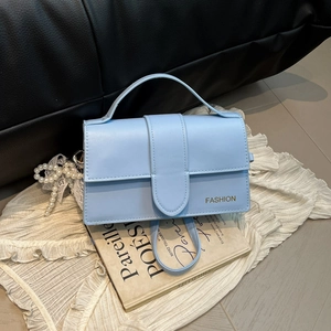 Elegant light blue square handbag with top handle and pearl charm on white fabric background