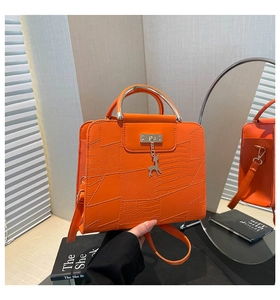 Detail van oranje tas met textuur, metalen handvat en decoratieve hertenhanger