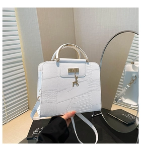 Detail van witte getextureerde tas met gouden ronde handgreep en hertenbedeltje op spiegels