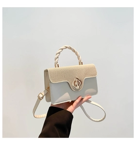 Close-up of woven straw and white leather flap bag with a golden floral twist lock