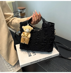 Detail of black pleated bucket bag with a cute plush bear charm and crossbody strap