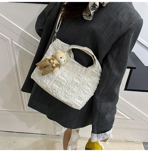 Detail of white pleated bucket bag with cute bear charm and thin shoulder strap