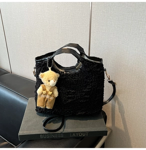 Detail of black pleated bucket bag featuring a cute plush bear charm and leather handles