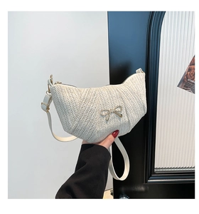 Detailed view of cream crescent straw bag with metallic bow charm and woven texture
