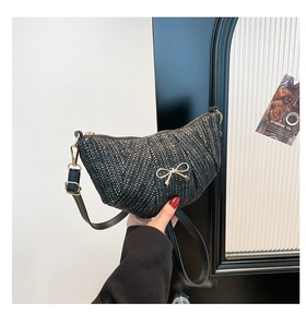 Close-up of black woven dumpling bag with golden bow accent and metal hardware detail