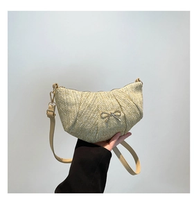 Close-up of woven straw crescent bag featuring a silver metal bow detail and slim strap