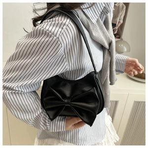 Détail du sac à main élégant en cuir noir mat avec grand nœud porté par le modèle