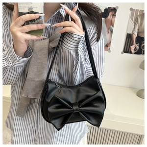 Détail d'un sac à bandoulière noir avec un grand nœud porté par un mannequin en tenue chic