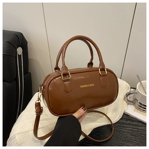 Detailed shot of dark brown cylindrical crossbody bag with gold hardware and leather handles
