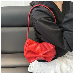 Détail d'un sac à bandoulière rouge en forme de nœud porté par un mannequin femme