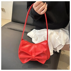 Détail du sac à main rouge avec nœud papillon, texture cuir et fermeture zippée