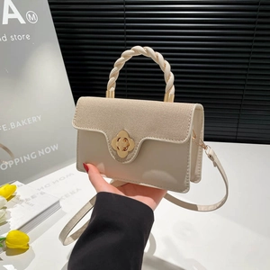 Elegant cream crossbody bag with woven flap and gold flower clasp shown in a chic studio