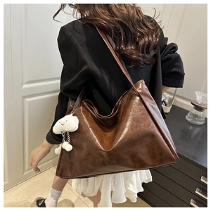 Detail of dark brown glossy leather tote bag featuring a white plush cloud charm accessory