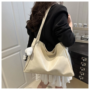 Detail of off-white leather tote bag with a soft heart pendant and shoulder strap