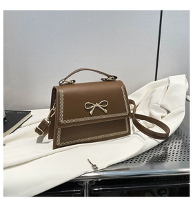 Detalle de bolso bandolera de cuero sintético marrón con lazo dorado y costuras en espiga