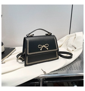 Detalle del bolso bandolera negro con hebilla de lazo dorado y bordes bordados