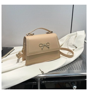 Detalle de bolso beige con hebilla de lazo dorado y bordes con costuras tejidas finas
