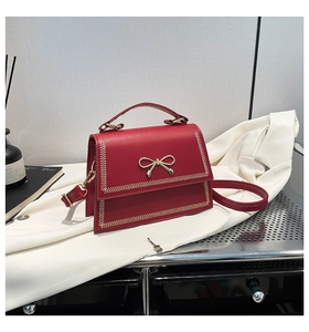 Detalle del bolso bandolera rojo con hebilla de lazo dorado y correa extraíble