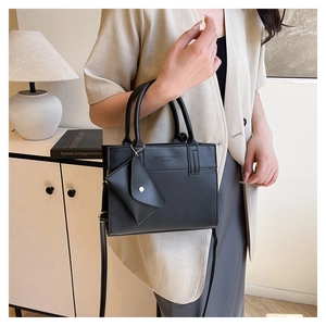 Detail of a chic black leather tote bag with a small triangular charm on a minimalist background