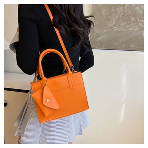 Detail of bright orange tote bag with mini pouch worn by model in striped outfit