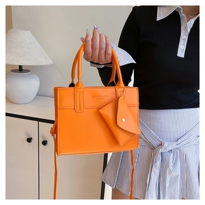 Detail of bright orange faux leather handbag set with matching envelope pouch and strap