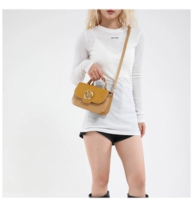 Close-up of khaki crossbody bag featuring woven texture flap and golden M buckle detail