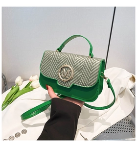 Detail of green woven crossbody bag featuring a golden M logo clasp and top handle