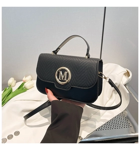 Detail of black crossbody bag featuring textured flap and elegant gold M metal buckle
