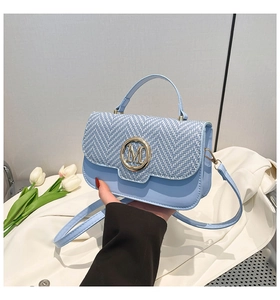 Detail of light blue handbag with woven texture and gold M logo in an elegant setup